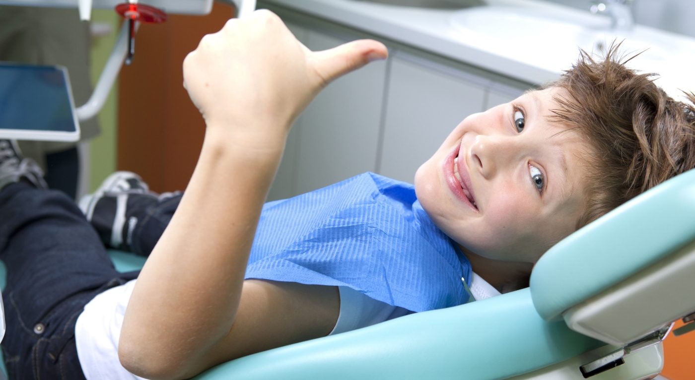 Smiling child giving thumbs up while visiting pediatric dentist