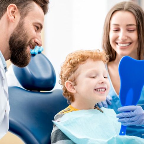 Dentist and dental assistant give child a mirror while he smiles