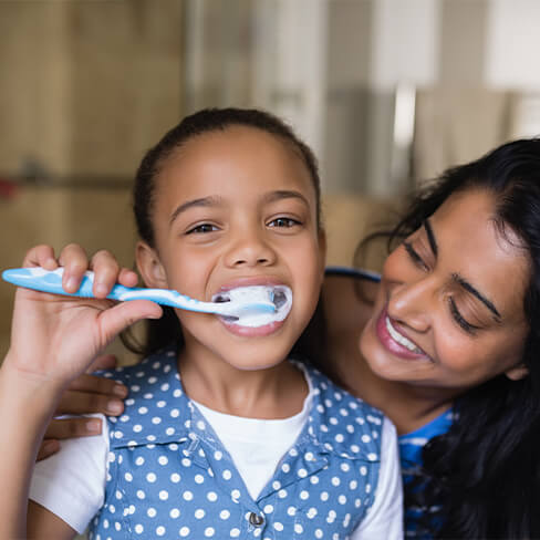 Mother helps child brush teeth to prevent dental emergencies