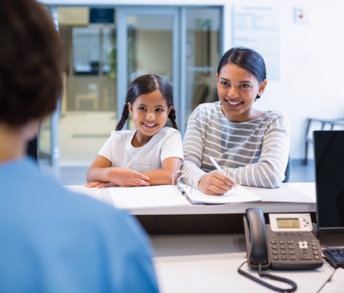 Mother and child filing out dental insurance paperwork at front desk of pediatric dental office