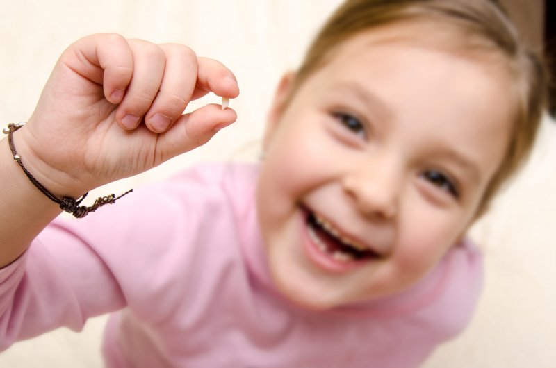 little girl holding baby tooth in hand