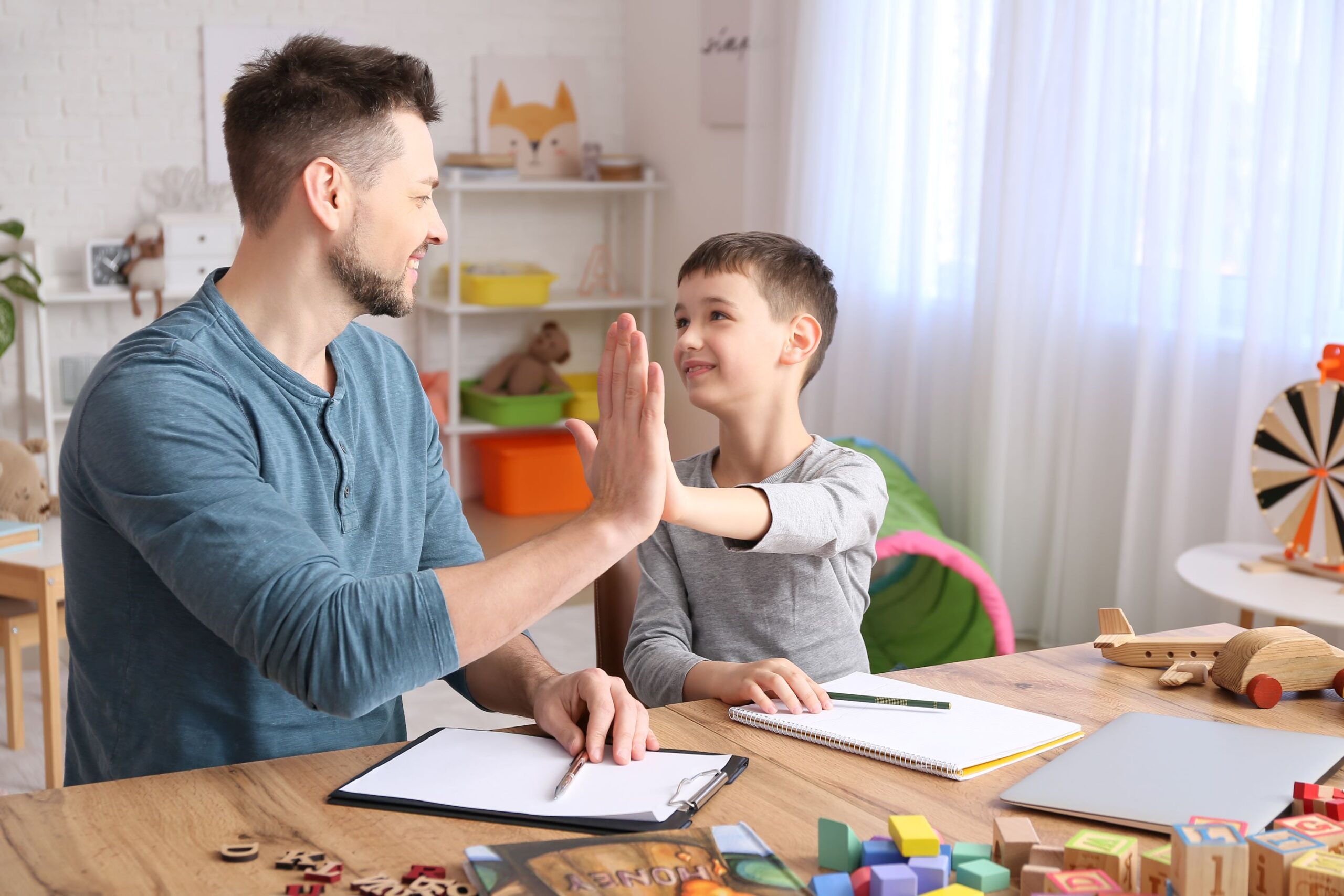 Man and boy with paper and pencils high-fiving at table.